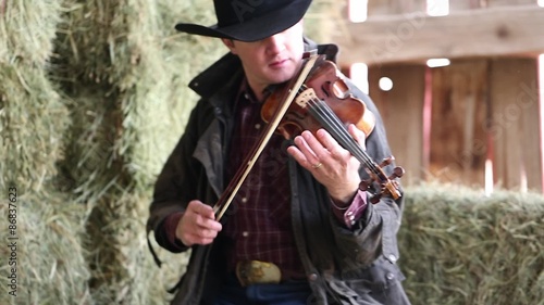 Cowboy tunes a violin in an old barn photo