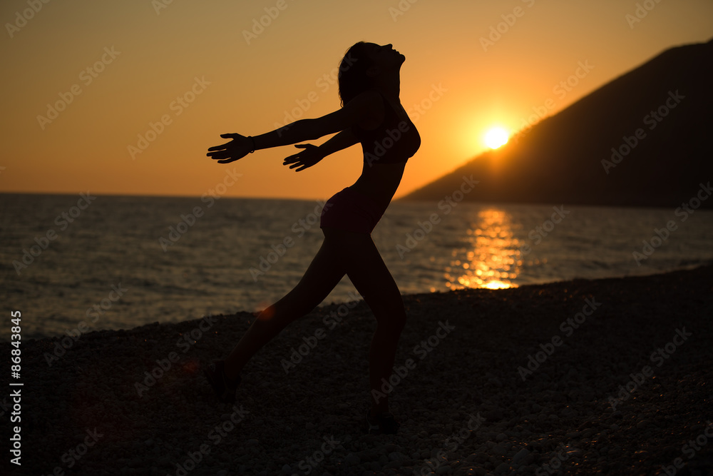 Carefree woman dancing in the sunset on the beach.Vacation vitality healthy living concept.Free woman enjoying sunset.Woman in embracing the golden sunshine of sunset,enjoying peace,serenity in nature