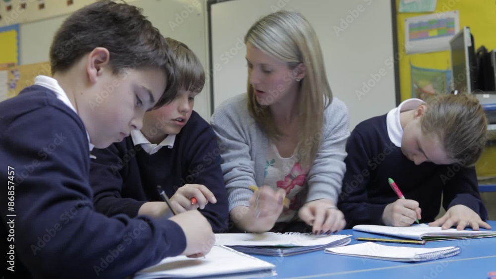 Pupils Working At Table With Teacher Helping Them Pupils Working At Table With Teacher Helping Them