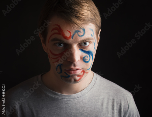 Portrait of young man with paint on his face on dark background.