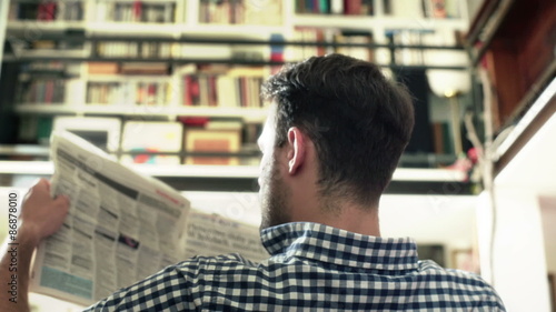 Man sitting back and reading newspaper downstairs
 photo