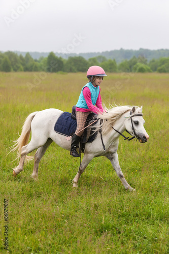 Beautiful baby girl on a white horse galloping across the field Outdoors