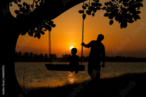 silhouette of father and son play swing under big tree the sunset