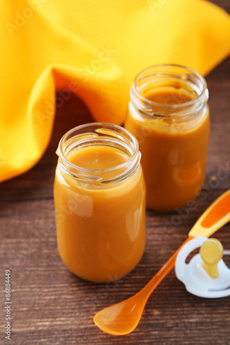 Baby food in bottles with spoon on brown wooden background