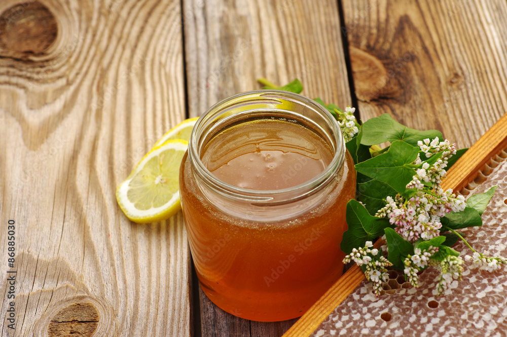 Honey in a glass jar, buckwheat flowers, a lemon and bee honeycombs in a summer sunny day. Honey with flowers and honeycombs Honey in a glass jar, buckwheat flowers, a lemon and bee honeycombs in a summer sunny day. Honey with flowers and honeycombs