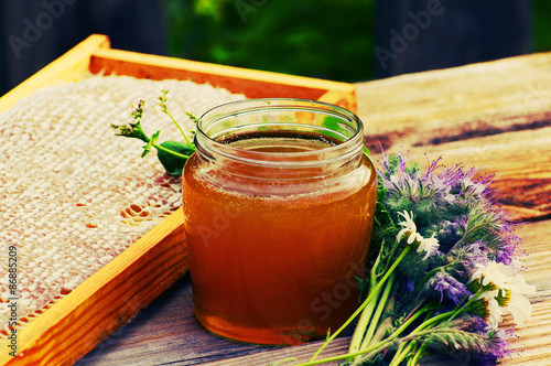 Honey in a glass jar and bee honeycombs with flowers melliferous herbs on a wooden surface. Honey with flowers. photo