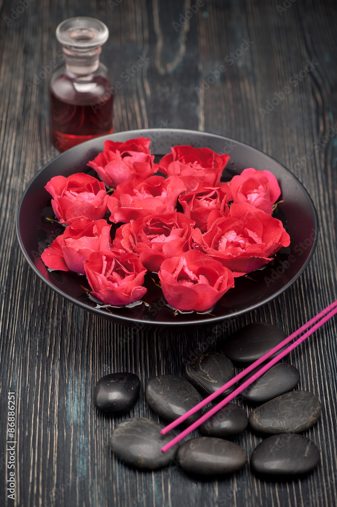 Spa, aromatherapy and body care. Bowl with flowers roses, black stones and rose oil.