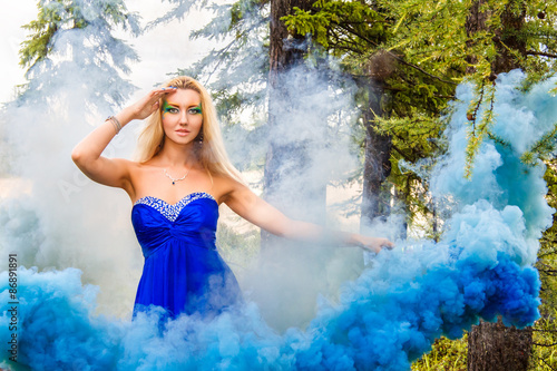 Beautiful young woman in a cloud of a bright blue smoke