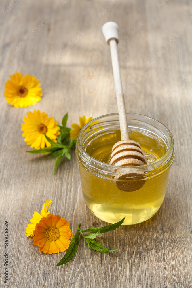 Linden honey in jar and calendula blossoms on wooden table, selective focus Linden honey in jar and calendula blossoms on wooden table, selective focus