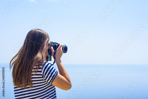 young caucasian female with camera on a cliff, woman taking photos on seaside