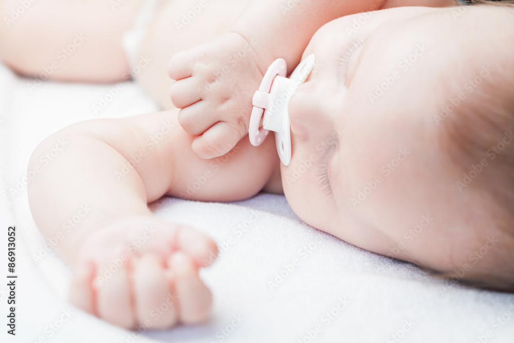 Newborn baby sweet sleeping on a white bed and sucks pacifier. Concept of baby care Newborn baby sweet sleeping on a white bed and sucks pacifier. Concept of baby care