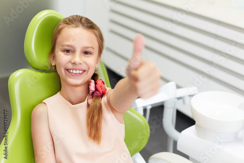 Portrait of happy girl shows thumb up gesture at dental clinic #86929477
