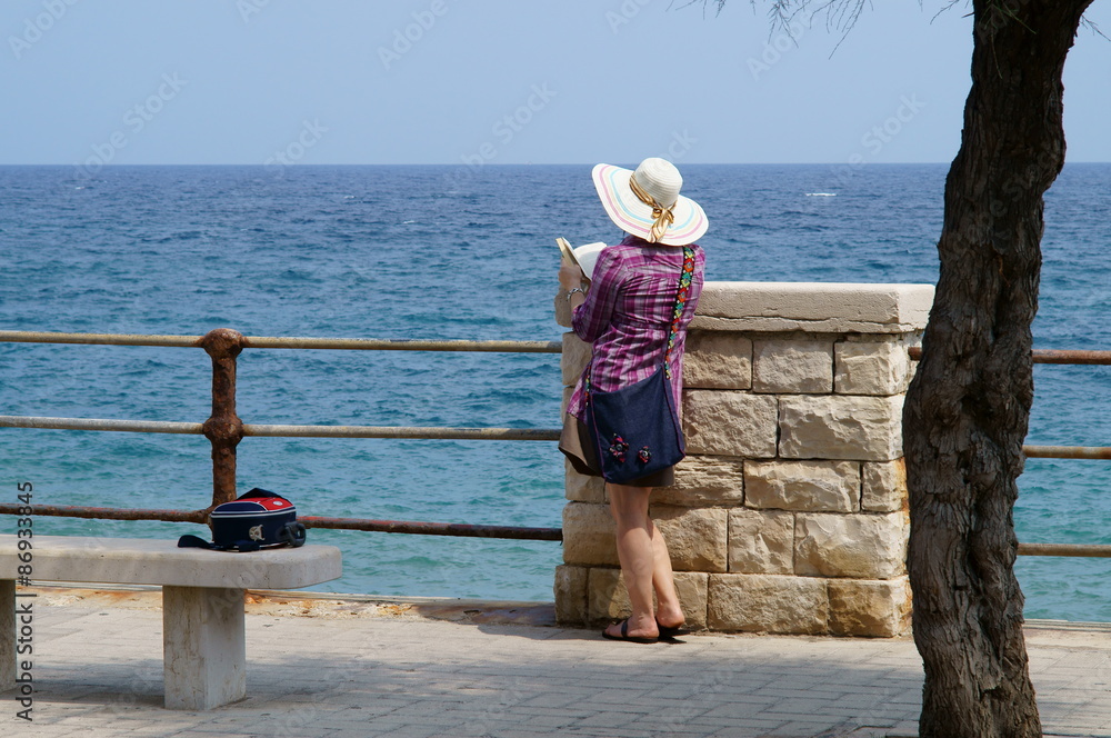Donna col cappello e libro in riva al mare