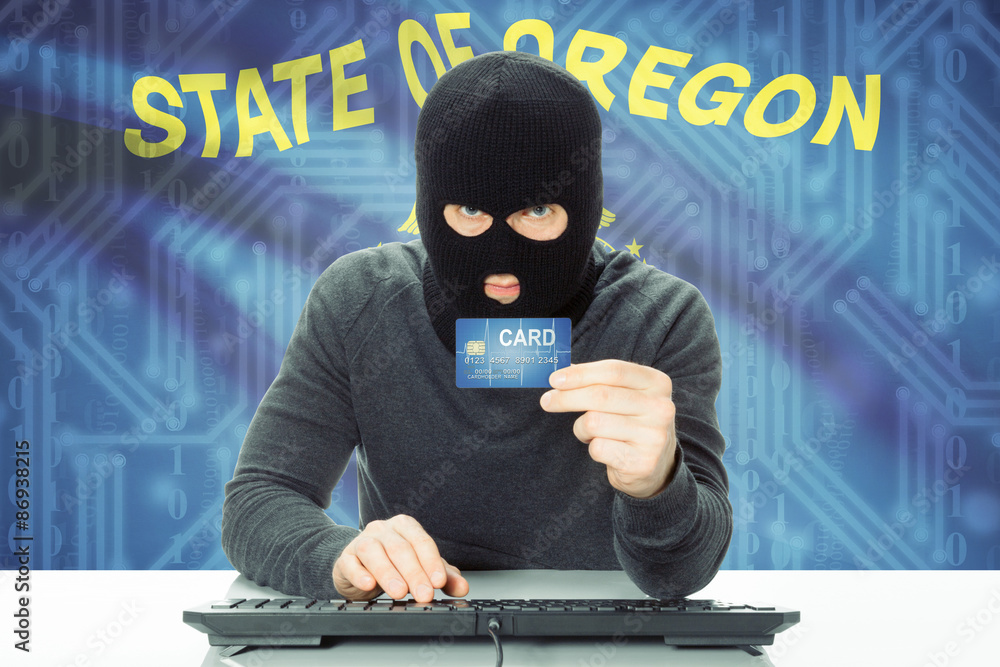 Hacker holding credit card and USA state flag on background - Oregon Hacker holding credit card and USA state flag on background - Oregon