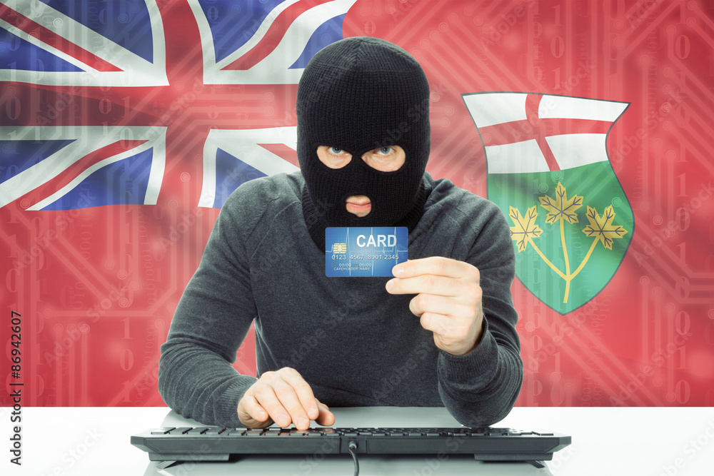 Hacker holding credit card and Canadian province flag on background - Ontario Hacker holding credit card and Canadian province flag on background - Ontario