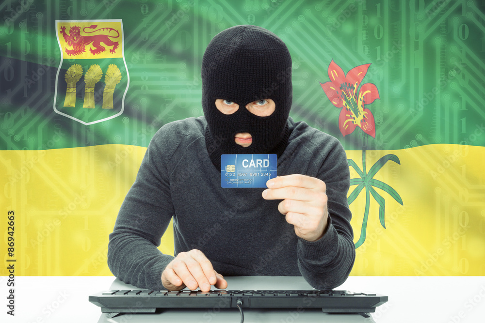 Hacker holding credit card and Canadian province flag on background - Saskatchewan Hacker holding credit card and Canadian province flag on background - Saskatchewan