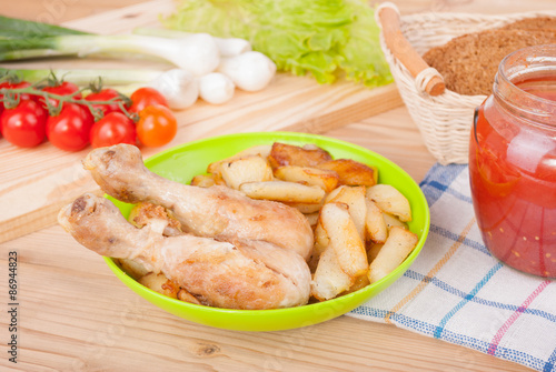 Chicken legs and fries on the plate on the kitchen table.