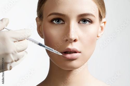 Beautiful girl doing an injection to increase the lips on a white background