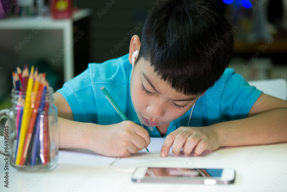 Naklejka premium A boy using cellphone and painting on a white paper at home