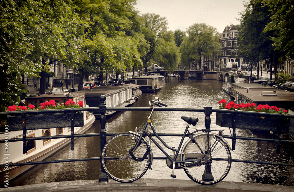 Naklejka premium Rower zaparkowany na moście dla pieszych Z widokiem na kanał w Amsterdamie