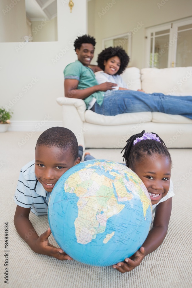 Fototapeta premium Happy siblings lying on the floor holding globe