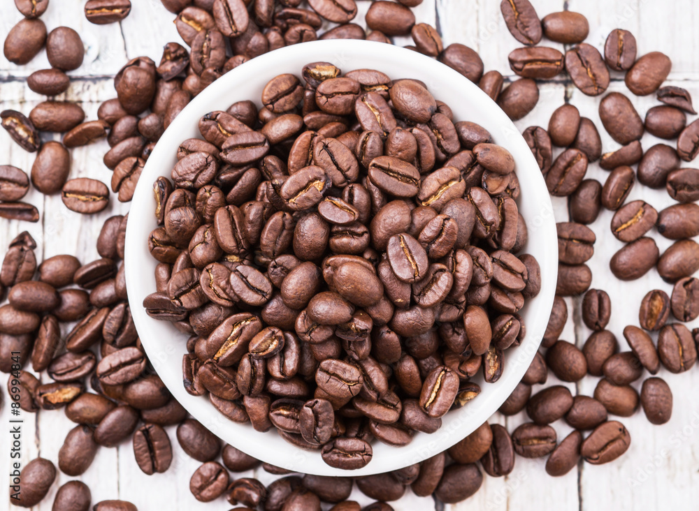 Roasted coffee beans in white bowl over rustic wooden background Roasted coffee beans in white bowl over rustic wooden background