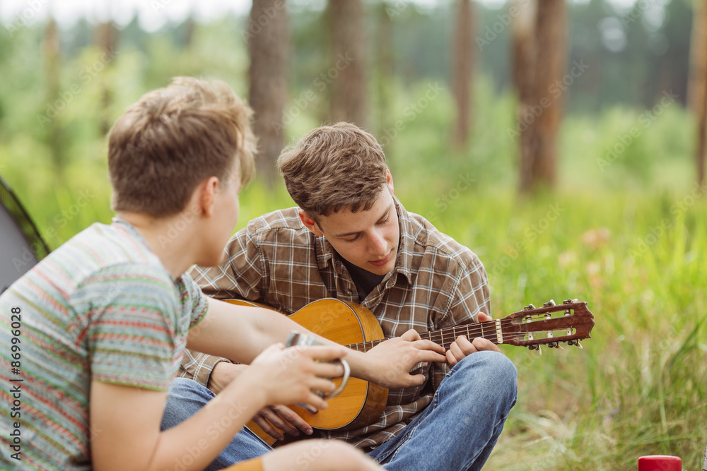 Two friend sitting in the tent, play the guitar and sing songs