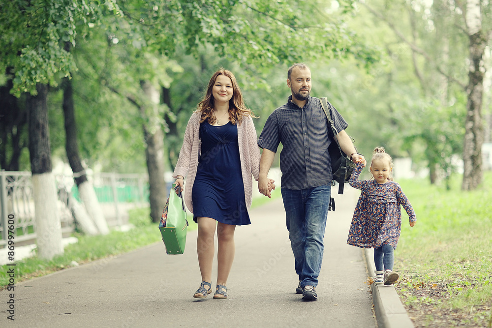 Mom and young daughter and dad, a young family on a walk in the park in summer Mom and young daughter and dad, a young family on a walk in the park in summer