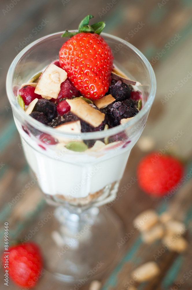 Homemade granola with Greek yoghurt topped with frozen berries, coconut and a fresh strawberry.Served in a tall glass. Homemade granola with Greek yoghurt topped with frozen berries, coconut and a fresh strawberry.Served in a tall glass.