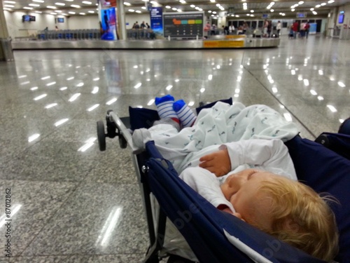 Baby sleeps in stroller while waiting for bags at an airport photo