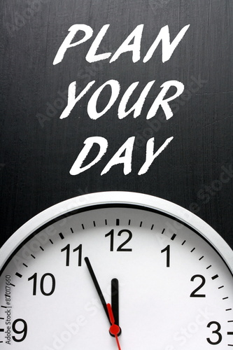 The phrase Plan Your Day in white text on a blackboard avove a modern wall clock