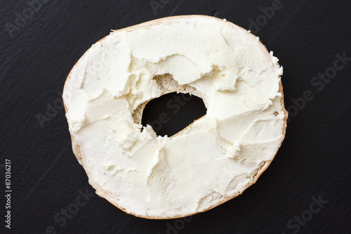 Bagel spread with cream cheese. Isolated on black wood from above.