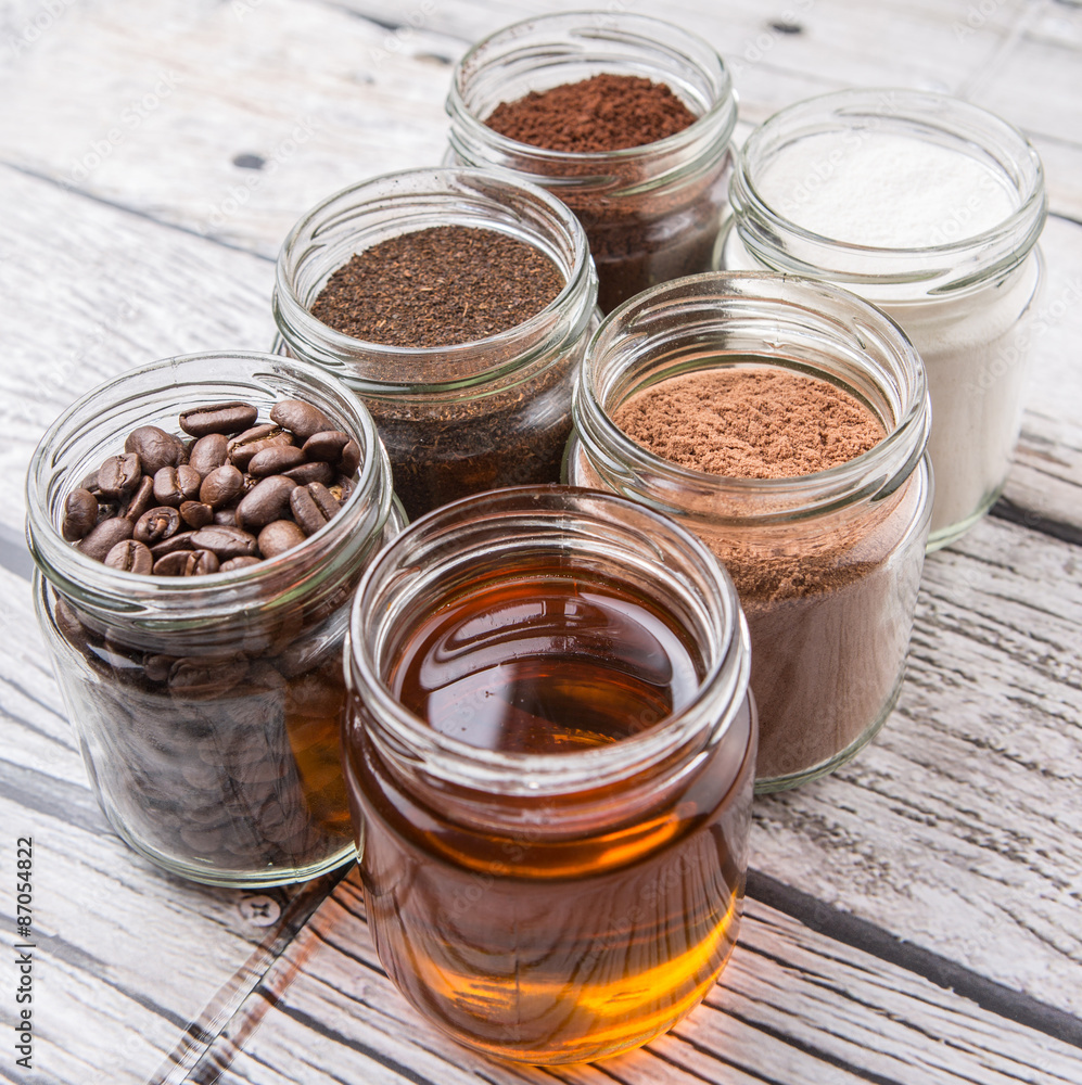 Coffee beans, coffee powder, creamer, cocoa powder, honey and processed tea leaves in a mason jar over weathered wooden background Coffee beans, coffee powder, creamer, cocoa powder, honey and processed tea leaves in a mason jar over weathered wooden background