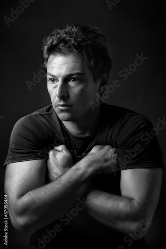 Black and white low key portrait of beautiful and mysterious man with crossed arms. Rembrandt light