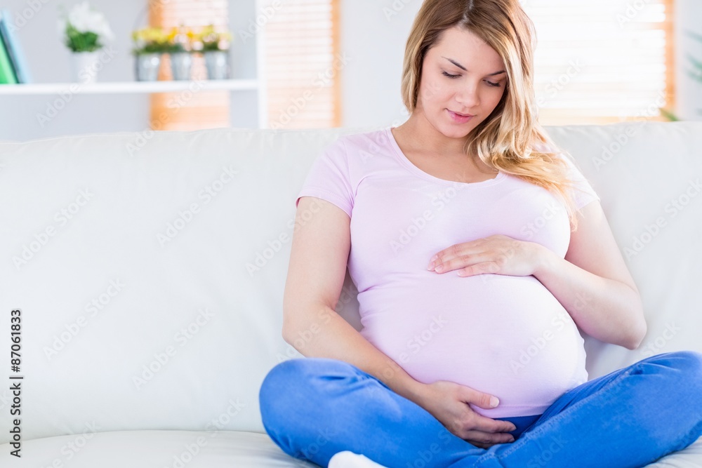 Pregnant woman sitting on couch touching her belly Pregnant woman sitting on couch touching her belly