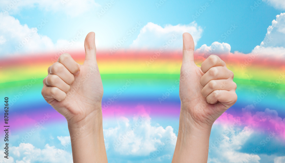 hands showing thumbs up over rainbow in blue sky hands showing thumbs up over rainbow in blue sky