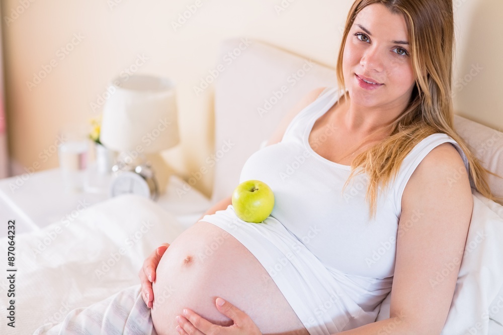 Pregnant woman lying on bed with apple in belly Pregnant woman lying on bed with apple in belly