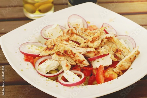 Greek salad with grilled turkey on wooden table
