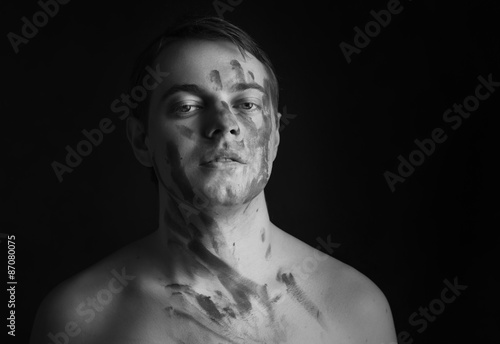 Young man with grey paint on his face on dark background.