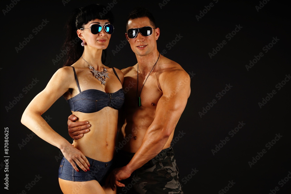 Muscular man in sunglasses with his girlfriend on dark background, right you can write some text