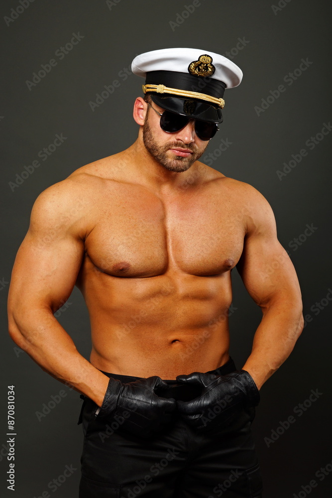 Muscular man in captain cap with sunglasses on gray background