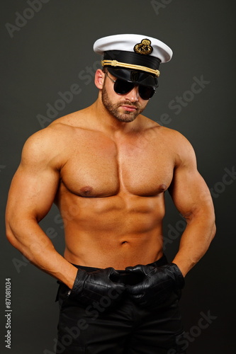 Muscular man in captain cap with sunglasses on gray background