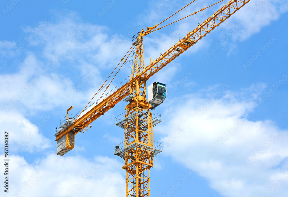 Yellow construction tower crane against blue sky Yellow construction tower crane against blue sky