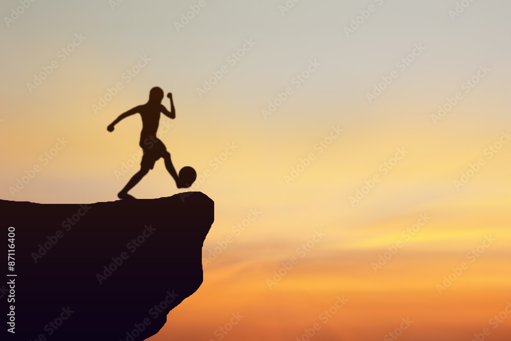Children kick soccer silhouette standing on a cliff. Sunset background