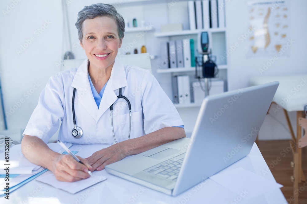 Happy doctor looking at camera and writing on clipboard Happy doctor looking at camera and writing on clipboard