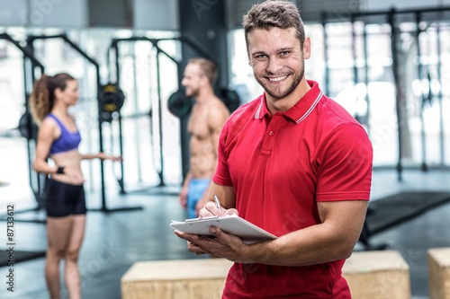 Smiling muscular trainer writing on clipboard