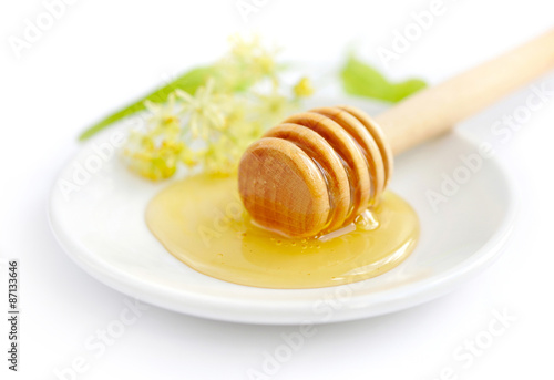 Honey dipper with honey with flowers of linden on white saucer