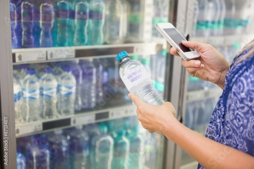 Woman comparing the price of a bottle of water with her phone