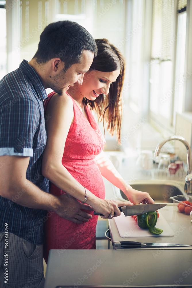 Young couple cooking together in the kitchen while man embracing his pregnant wife Young couple cooking together in the kitchen while man embracing his pregnant wife