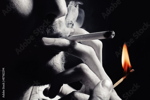 Men's hand lights a cigarette with a match